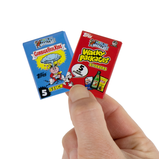 A hand holds the Micro Card Sticker packs, one Garbage Pail Kids and the other Wacky Packages.