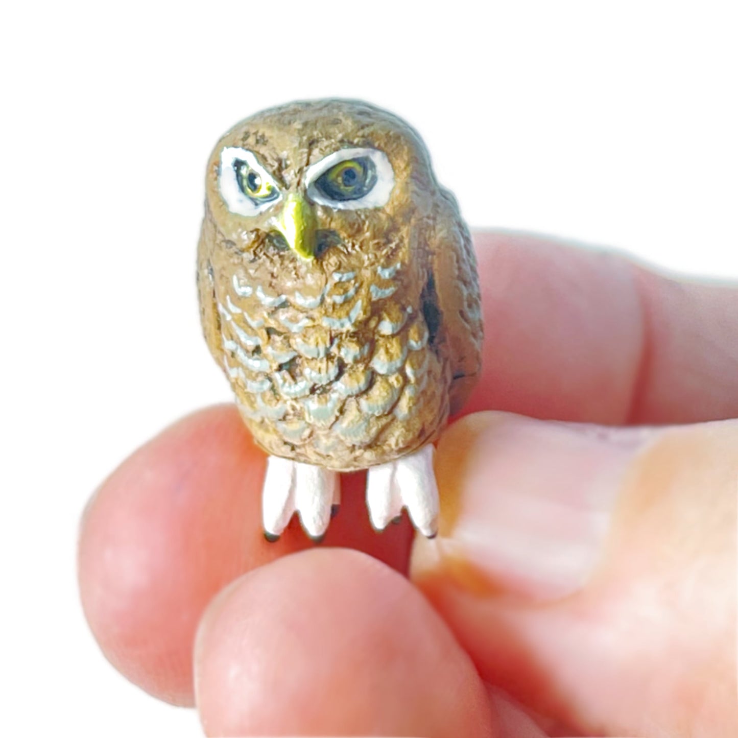 A hand holds a tiny brown toy owl figurine.