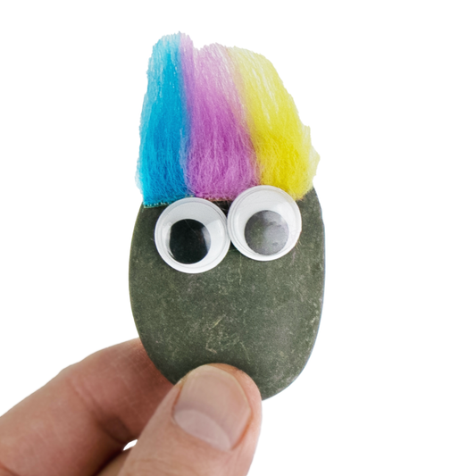 A hand holding a World's Smallest Original Pet Rock with googly eyes and colorful hair 