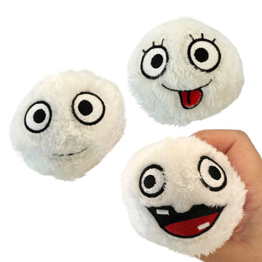 A hand holds a silly faced snowball plush toy and two other snowball plushies are pictured.