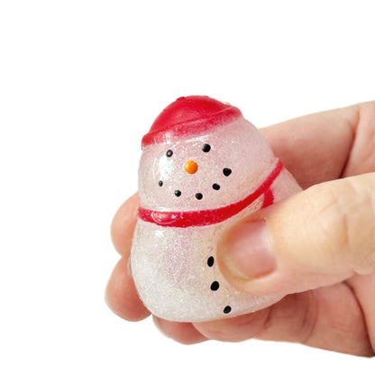 A hand holding a small glittery squishy snowman fidget toy wearing a red hat and scarf.