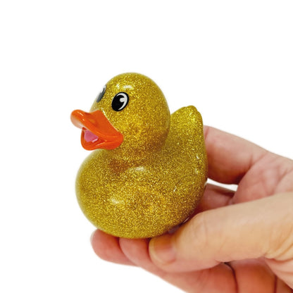 A hand holds a glittery gold rubber duck toy.