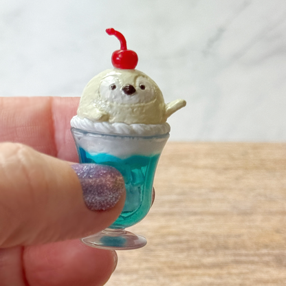 A hand holds a cream soda seal tiny toy dessert with a cherry on top