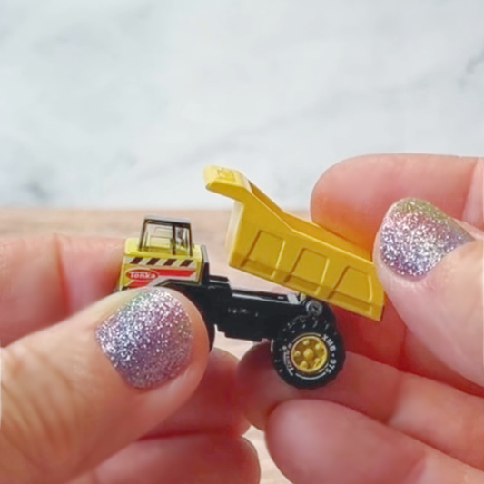 Hands hold the World's Smallest Tonka Toy Dump Truck with moveable dump and working wheels. 