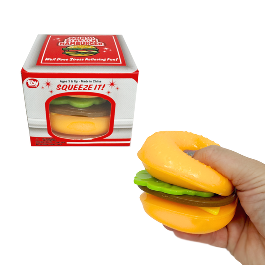 A hand holds a squishy burger sensory toy while one in the box sits behind.