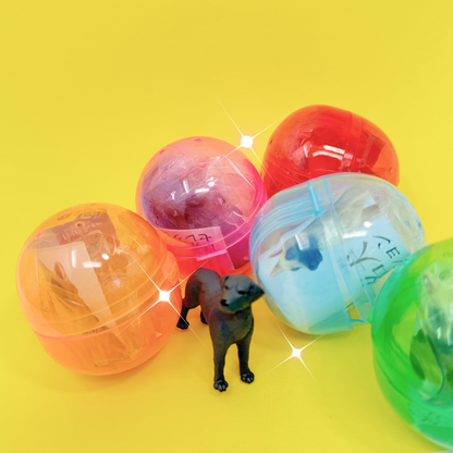 A tiny toy black lab stands in front of the colorful gachapon balls of World Famous Dogs