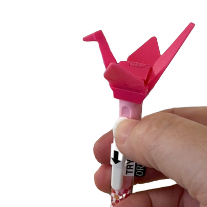 A hand is pushing the button to flap the wings of the pink origami ballpoint pen