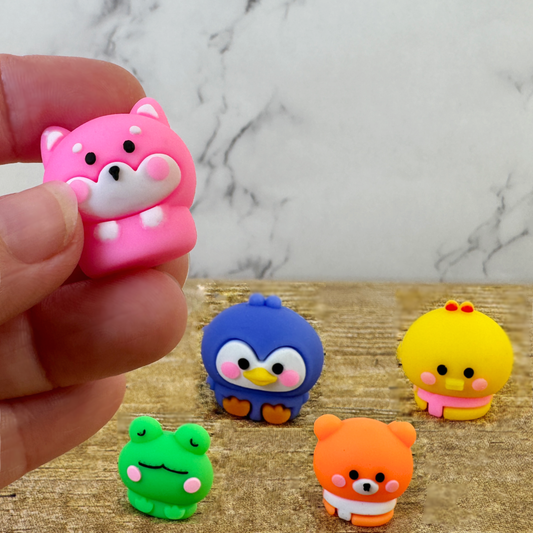 A hand holds a pink puppy eraser while 4 other cute animal shaped erasers sit on the table.
