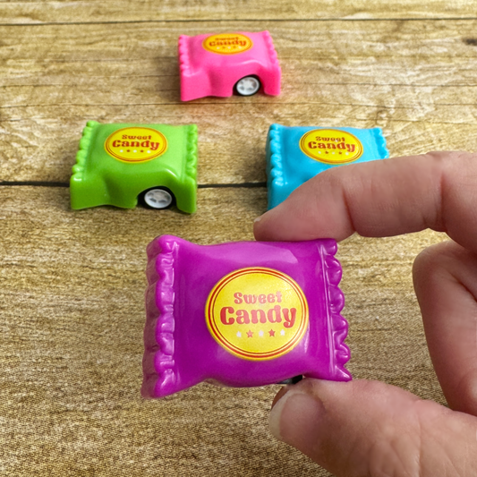 A hand holds a purple candy shaped toy car while 3 others lay on the table.