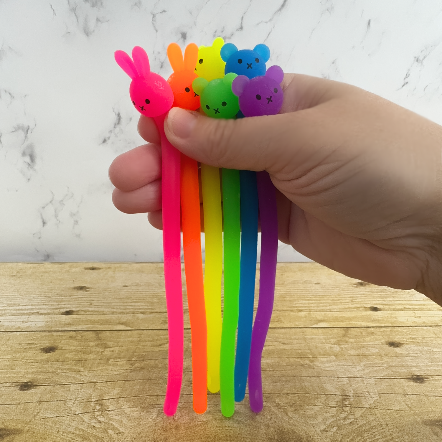 A hand holds a rainbow collection of noodle fidgets, they have bear or bunny heads. 