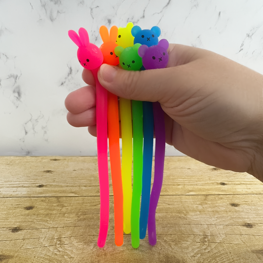 A hand holds a rainbow collection of noodle fidgets, they have bear or bunny heads. 