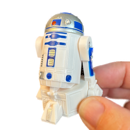 A hand holds an R2-D2 Star Wars droid toy gachapon.