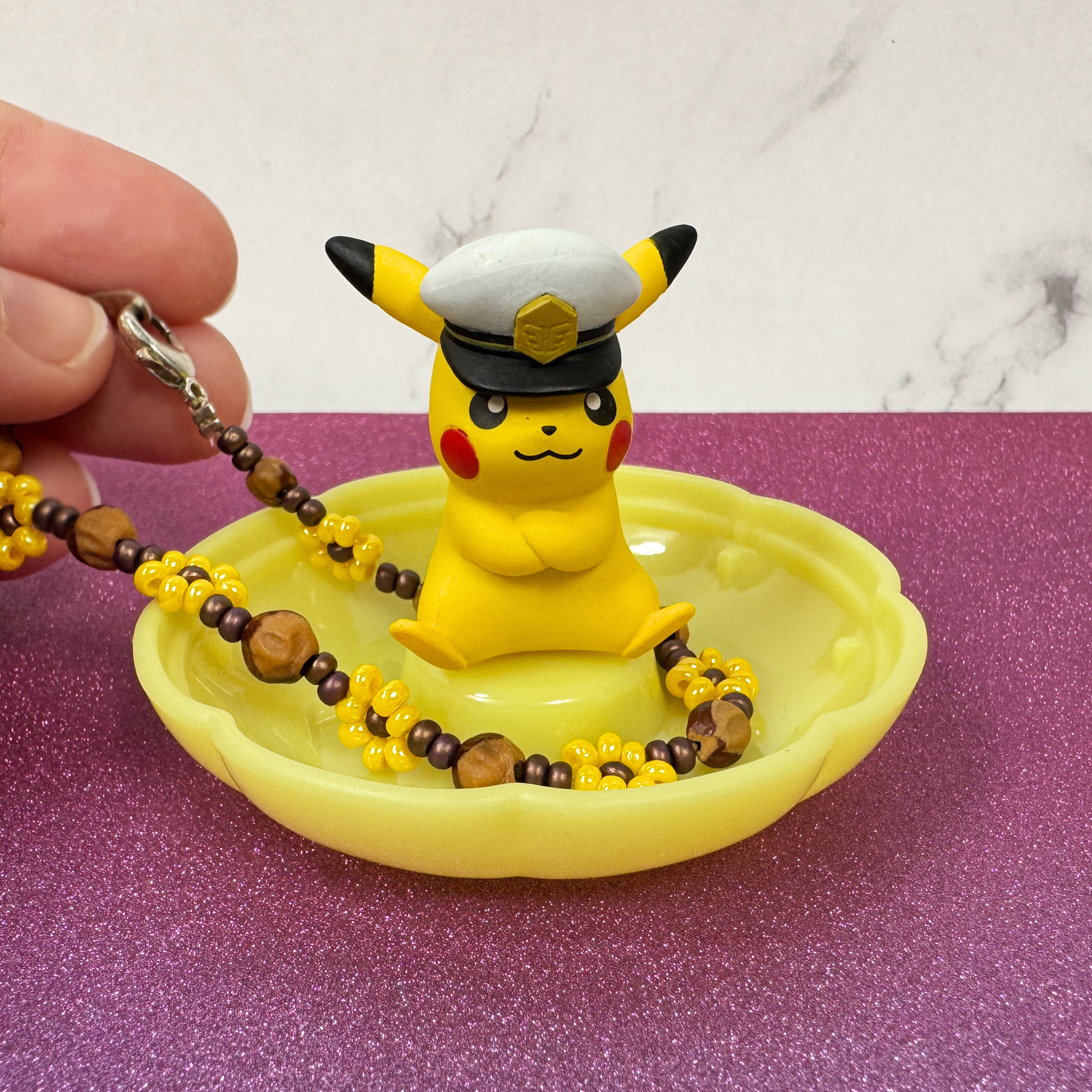 A hand puts a bracelet on the Pikachu Pokemon Gemries trinket tray.,