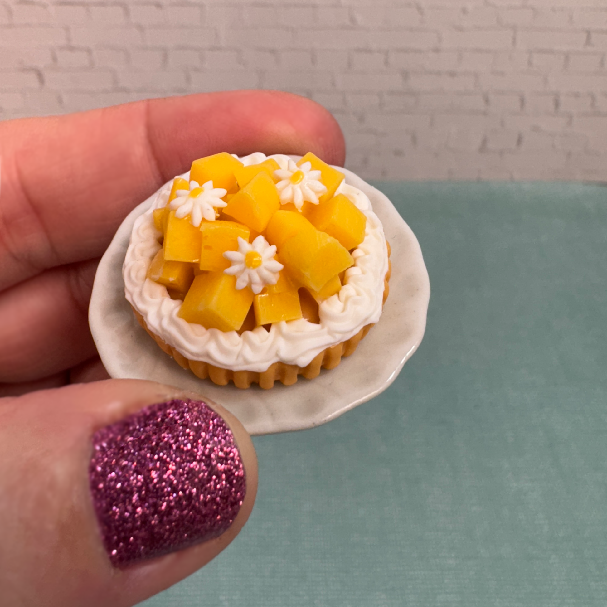 A hand holds a mini peach tart figure.