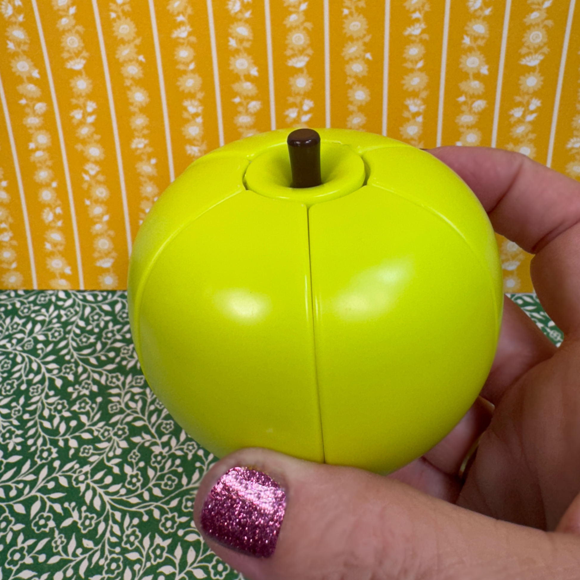 A hand holds a green apple shaped fidget toy.