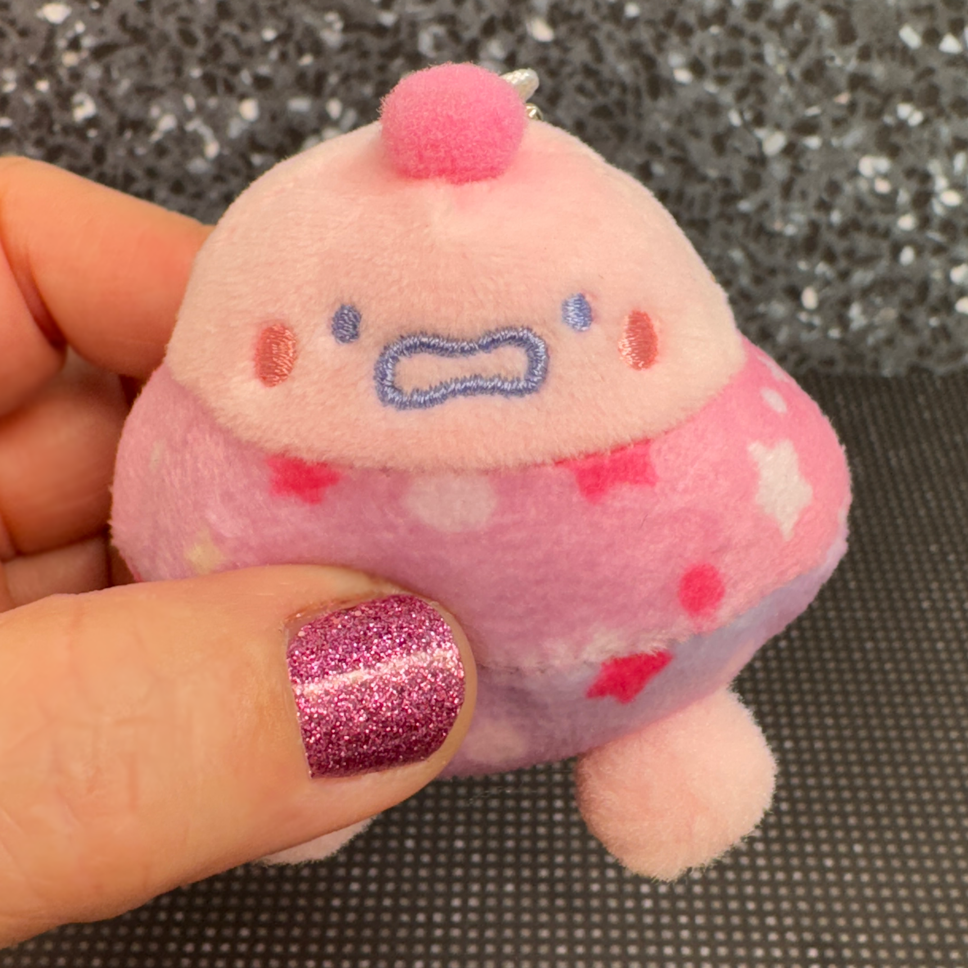 A hand holds a small pink plush toy UFO baby that looks nervous