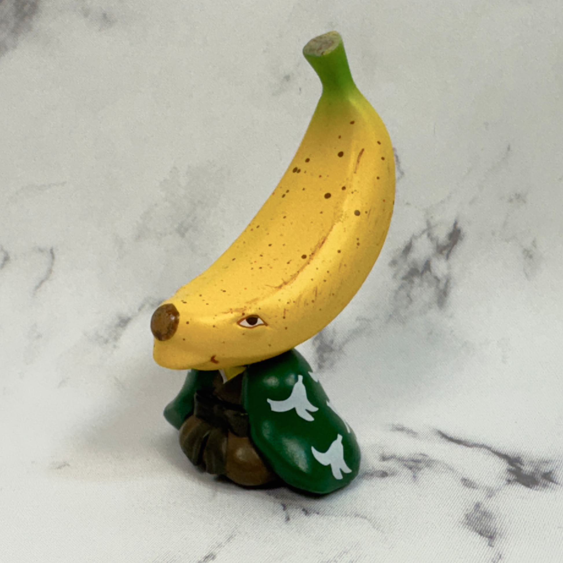 An opened capsule toy showing a fruit monster with a banana shaped head.