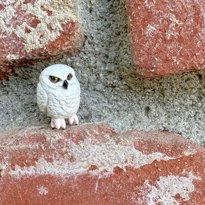 A very small white toy owl figurine on a brick wall.