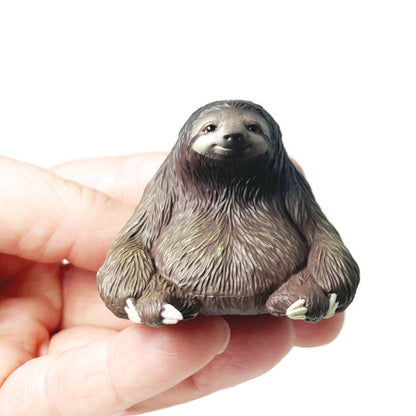 A hand holding a small Rben Studios toy sloth figurine.