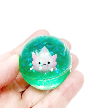 A hand holding a glittery green bouncy ball with a toy axolotl inside