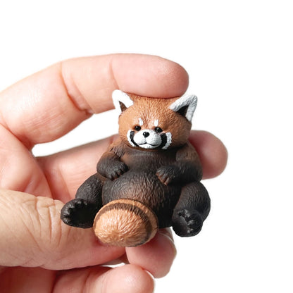 A hand holding a small Rben Studios toy red panda figurine.