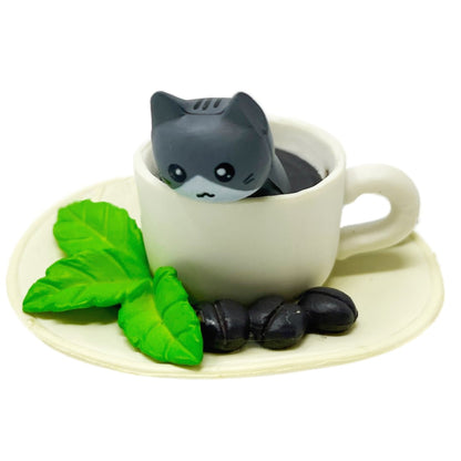 A toy figurine of a grey toy cat with a white toy coffee cup.