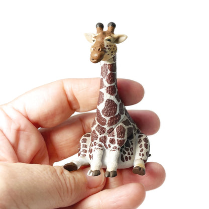 A hand holding a small Rben Studios toy giraffe figurine.