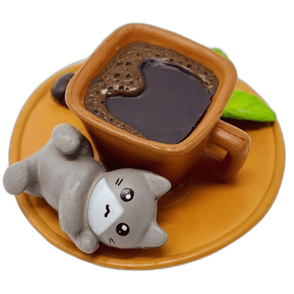 A toy figurine of a grey toy cat with a brown toy coffee cup.