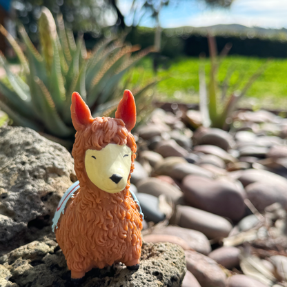 A brown toy alpaca or llama sits in nature