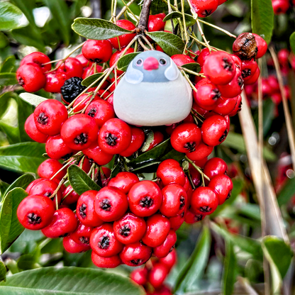 Tiny white bird figure sits in berry bush